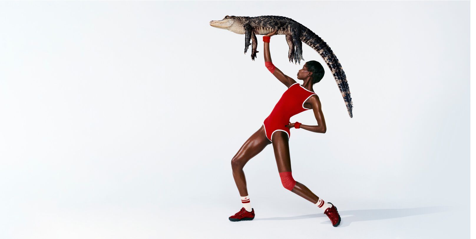 A woman in front of a white background wearing Gator Run shoes while holding an alligator